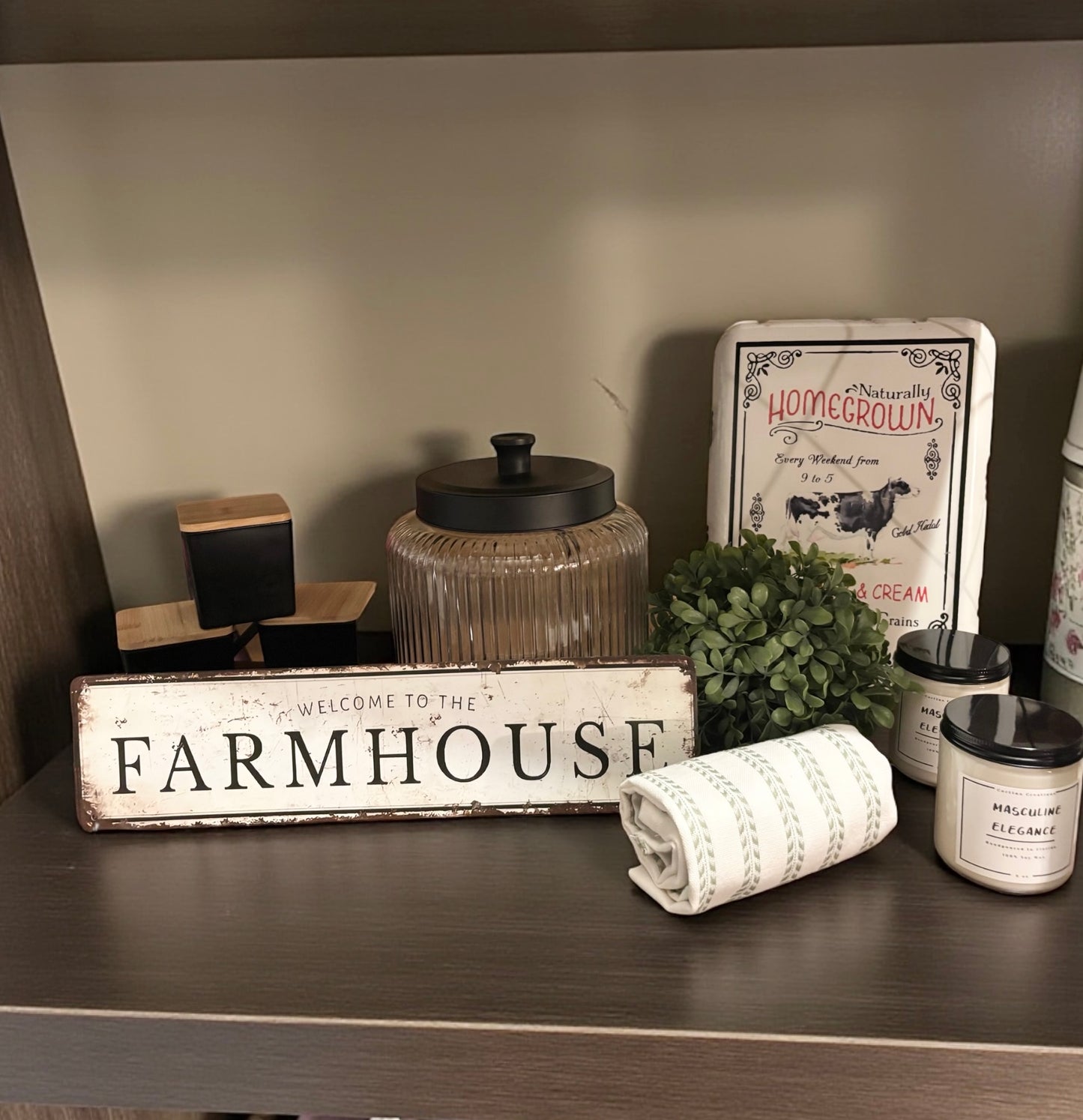 Decorative items on a shelf including a 'Farmhouse' sign, candles, and a plant.