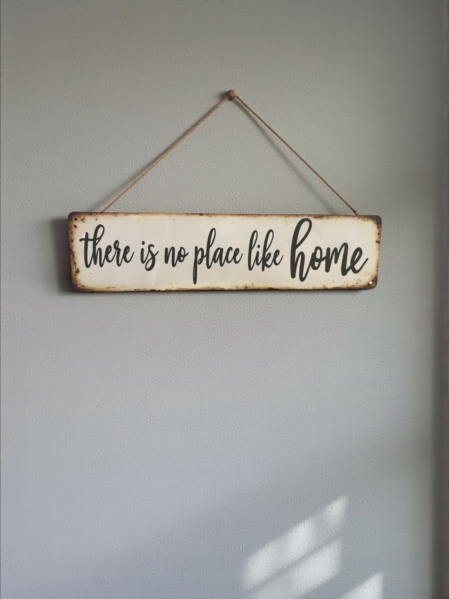 Decorative sign with 'there is no place like home' text on a plain wall.